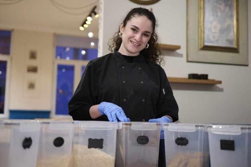 Una persona con delantal de chef negro y guantes azules, de pie detrás de una barra con recipientes transparentes. 2