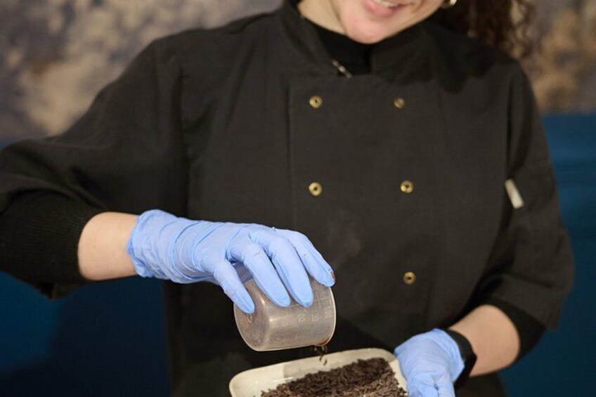 Una persona con un cappotto nero e guanti blu versa un liquido da un contenitore in una ciotola. 4