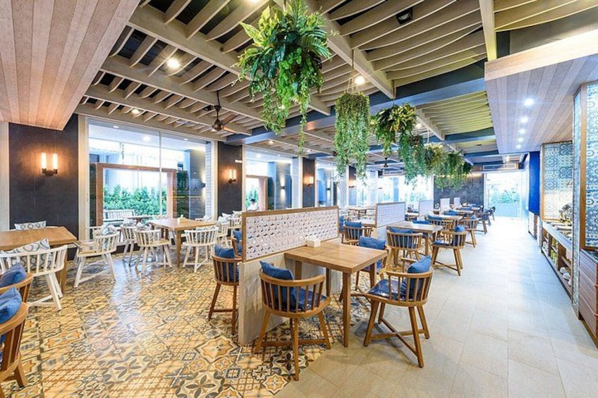 A restaurant interior with wooden tables and chairs, hanging plants, and patterned flooring. 5