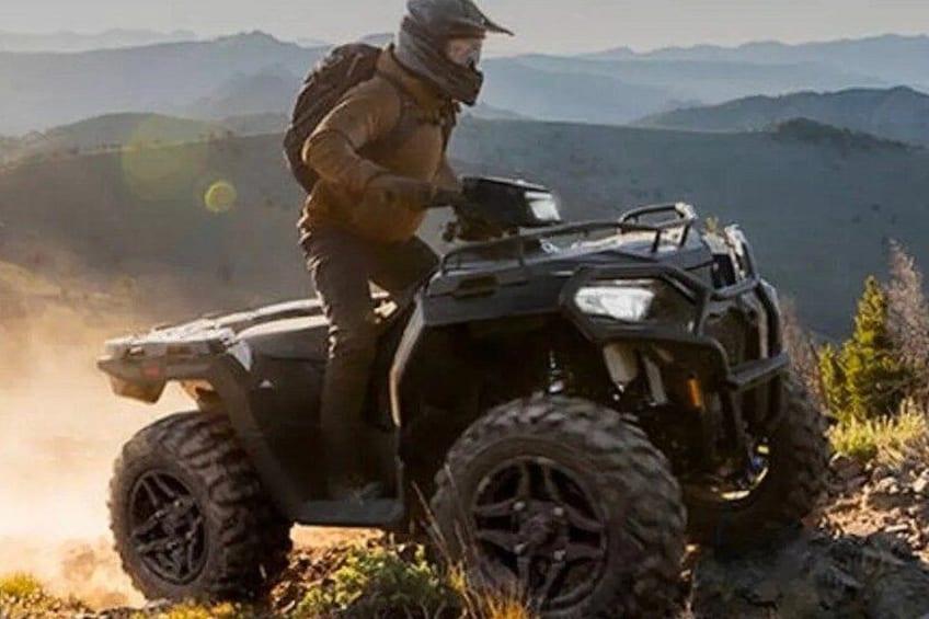 Une personne conduisant un quad sur un sentier de montagne et portant un sac à dos. 1