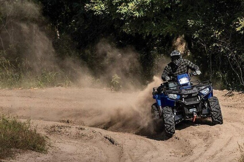 Una persona monta un cuatrimoto azul por un sendero de tierra rodeado de árboles. 3