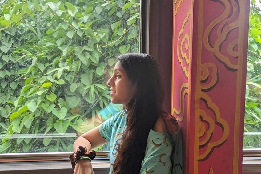 A person leaning against a window with a view of green foliage outside. 4