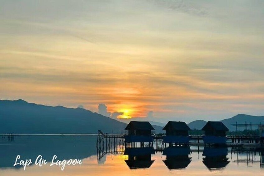 A sunset over a calm lake with overwater bungalows and mountains in the background. 1