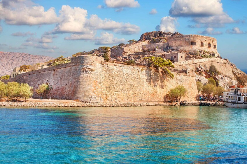 A historic stone fortress by a clear blue sea with a boat docked nearby. 5