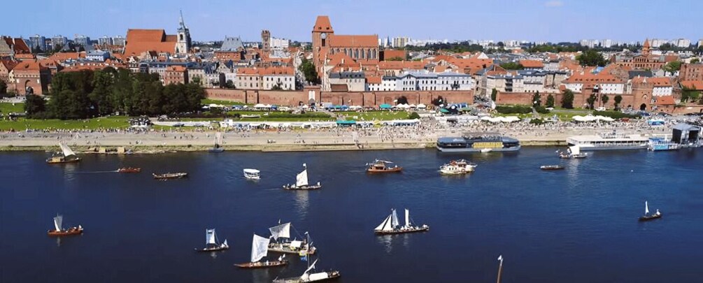 A coastal city with historic buildings, a harbor with sailboats, and a sandy beach. 1