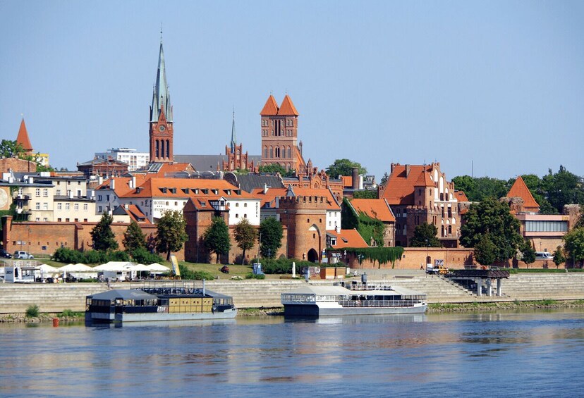 A riverside cityscape with historic buildings, a prominent church spire, and a castle tower. 3