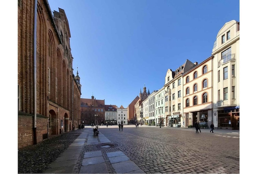 A cobblestone square with historic buildings, a clear blue sky, and a few pedestrians. 5