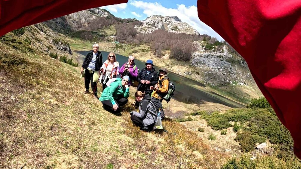 A group of hikers on a mountain trail with a lake and rocky mountains in the background. 1