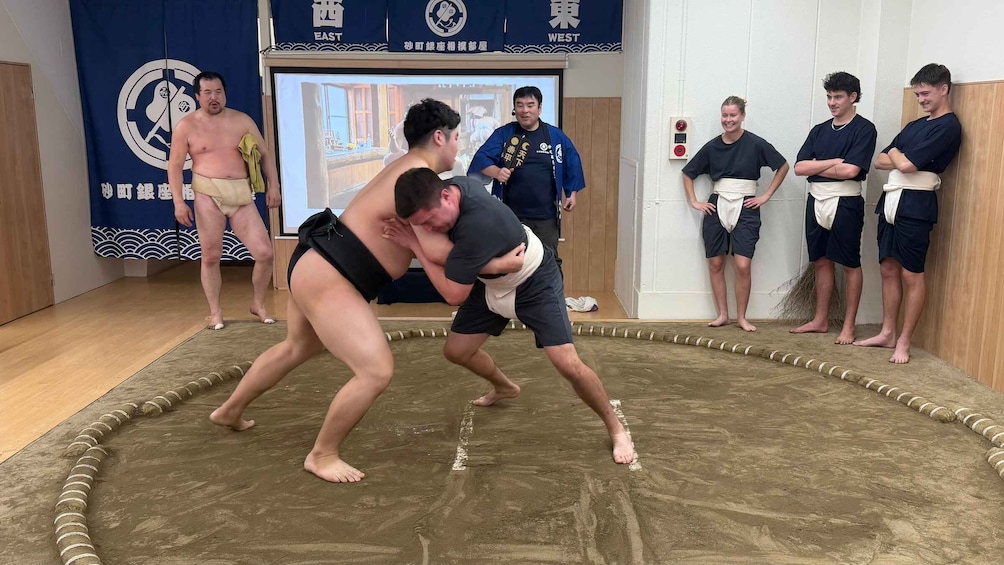 Two sumo wrestlers in a ring, with onlookers and a banner in the background. 1