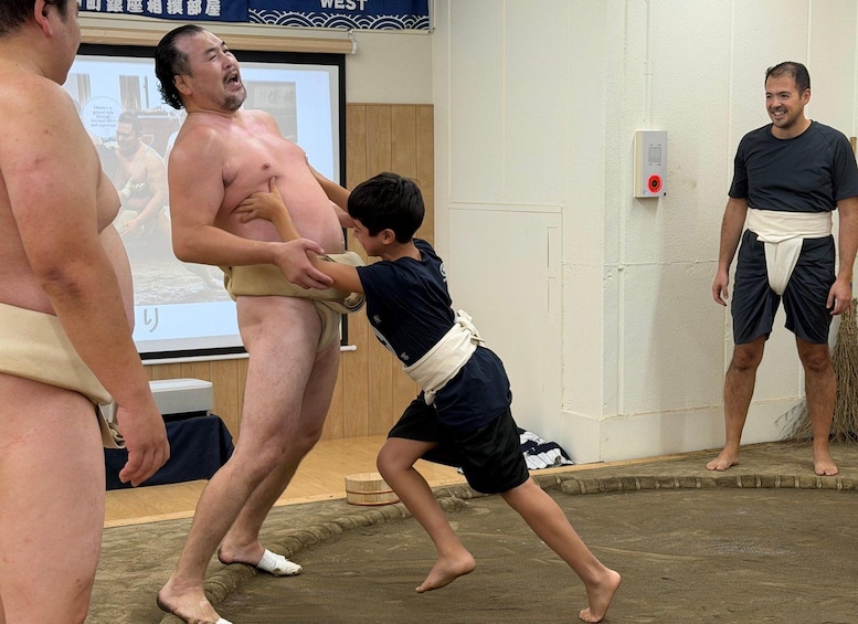 A sumo wrestling match with a child attempting to lift a sumo wrestler. 1