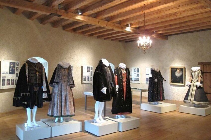 Mannequins displaying historical costumes in a museum with wooden beams and framed pictures on the walls. 5