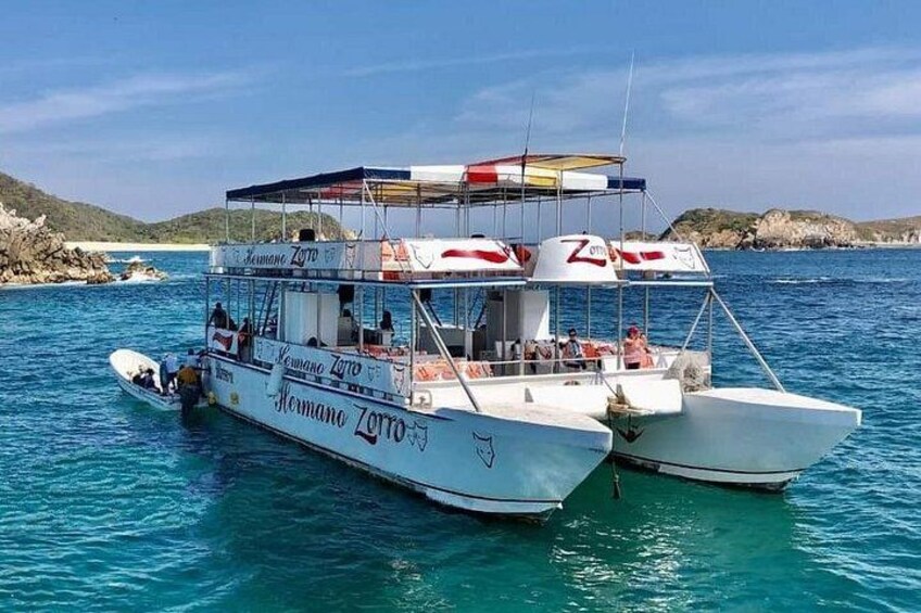 A boat named 'Hermano Zorro' anchored in clear blue waters with rocky hills in the background. 1
