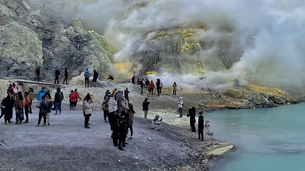 A group of people observing a geothermal area with steam and hot water. 5