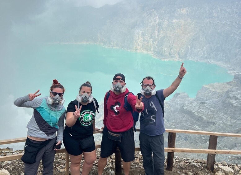 A group of people posing on a rocky overlook with a turquoise lake and mountains in the background. 3