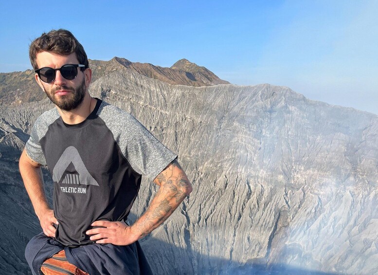 A person standing with hands on hips, wearing a black and gray athletic run t-shirt, in front of a mountainous landscape. 4