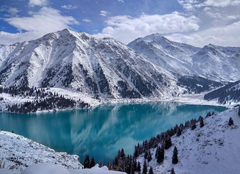 A snow-covered mountain range with a turquoise lake at its base. 3