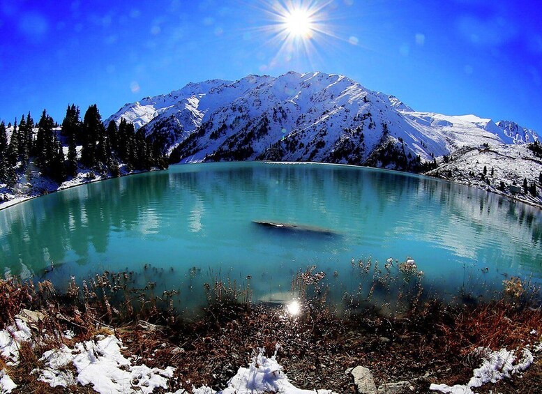 A clear mountain lake with snow-capped peaks and a bright sun in the sky. 4