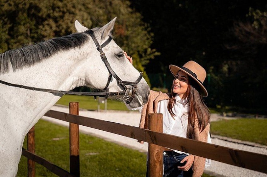 Een persoon leunt tegen een houten hek, naast een wit paard met een zwarte manen en staart. 3