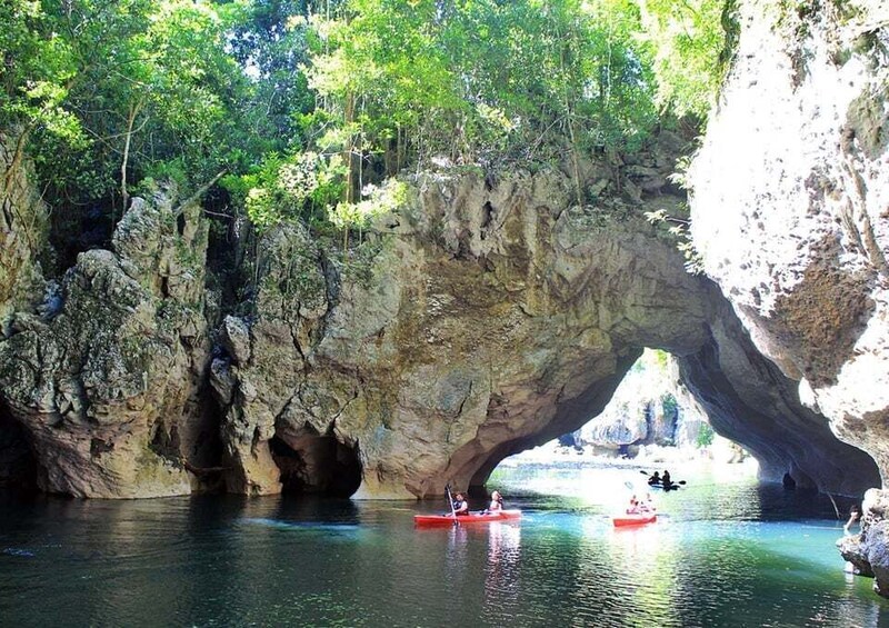 A natural rock arch over a calm river with kayaks. 3