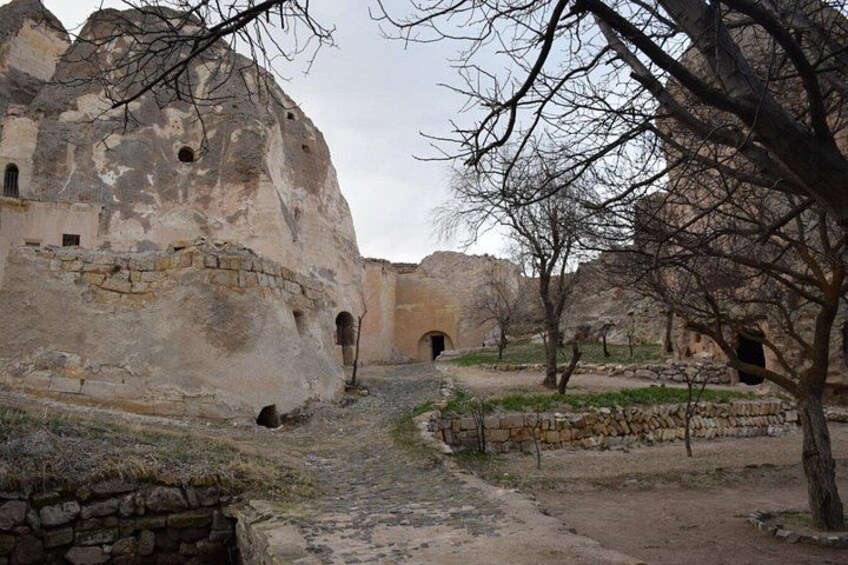 An ancient stone building with arched doorways, surrounded by bare trees and a dirt path. 2