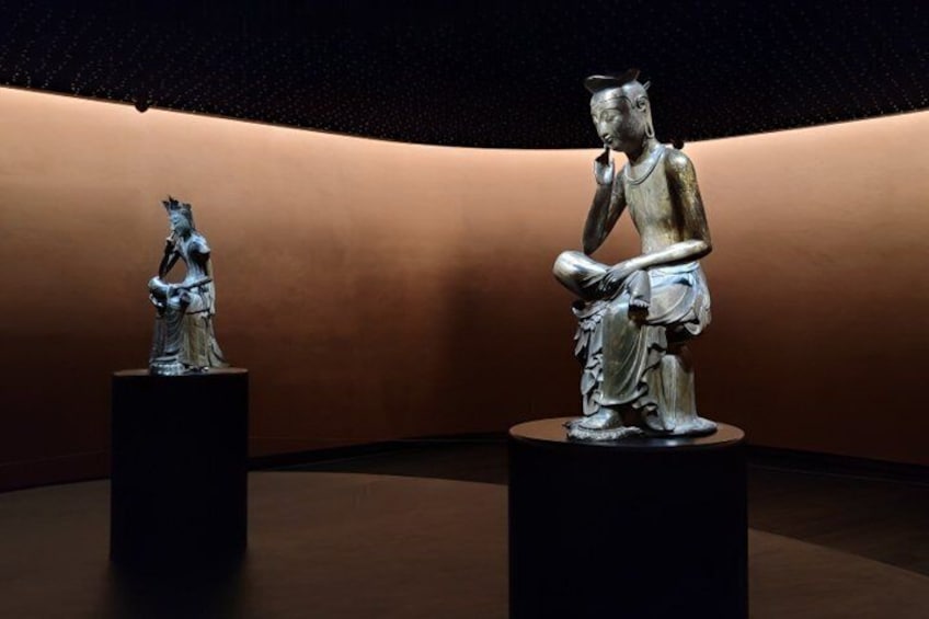Dos estatuas de bronce sobre pedestales en una habitación tenuemente iluminada, con una pared curva. 3