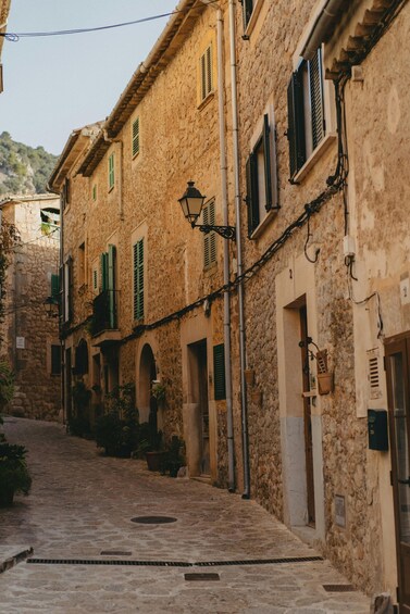 A narrow cobblestone street lined with historic stone buildings, green shutters, and a street lamp. 2