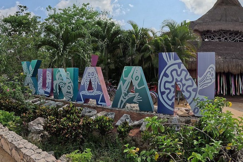 A tropical resort with thatched-roof huts, colorful signage with indigenous designs, and lush greenery. 3