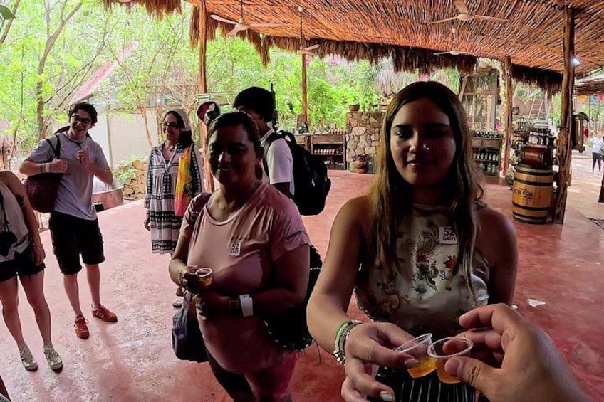 A group of people in an outdoor setting with a thatched roof structure, a stone wall, and a wooden barrel. 2