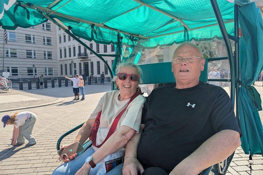 Twee personen zitten op een bank onder een groene luifel. 2