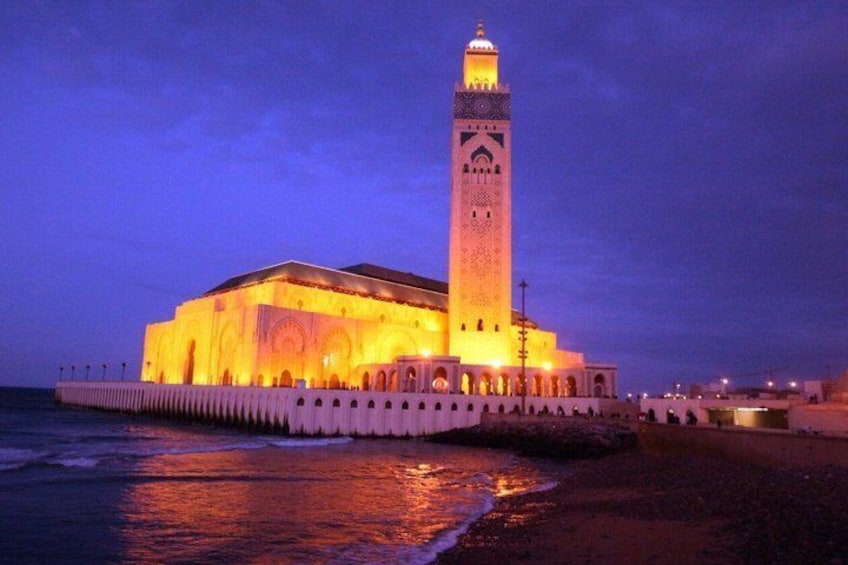 Ein beleuchtetes Gebäude mit einem hohen Turm am Meer bei Nacht. 2