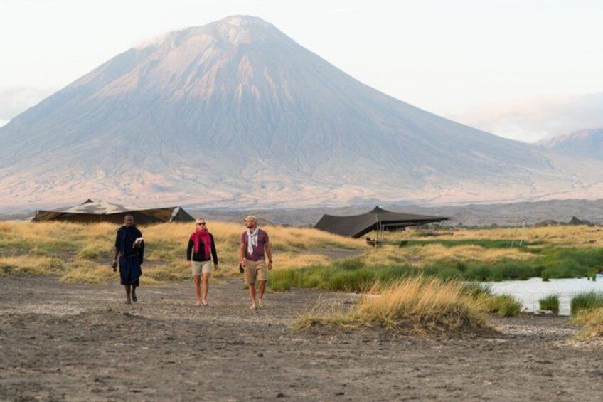 Three people walking on a dirt path with tents and a mountain in the background. 5