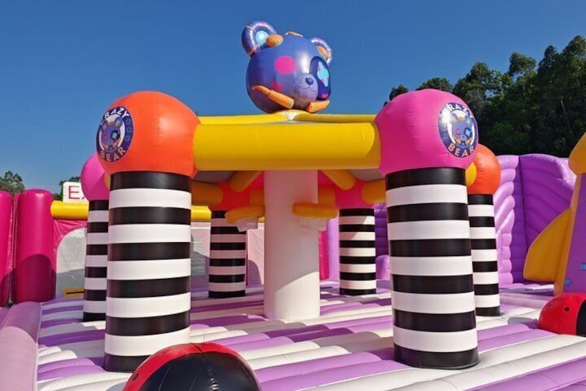 An inflatable play structure with a bear figure, striped columns, and a purple slide. 5