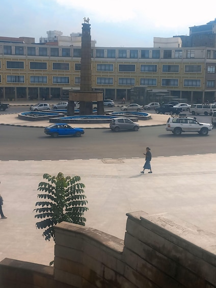 A parking lot with multiple cars, a central fountain, and a building with multiple windows in the background. 2