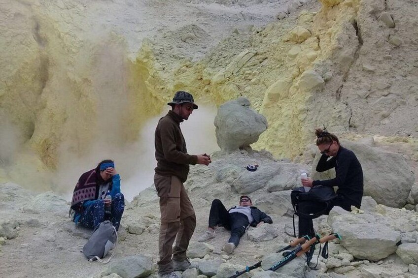 People sitting and standing near a yellowish cliff with a person holding a camera. 3