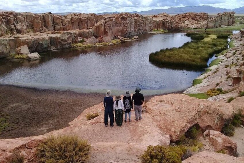A group of people standing on a rocky outcrop overlooking a calm body of water with a grassy area in the middle. 5