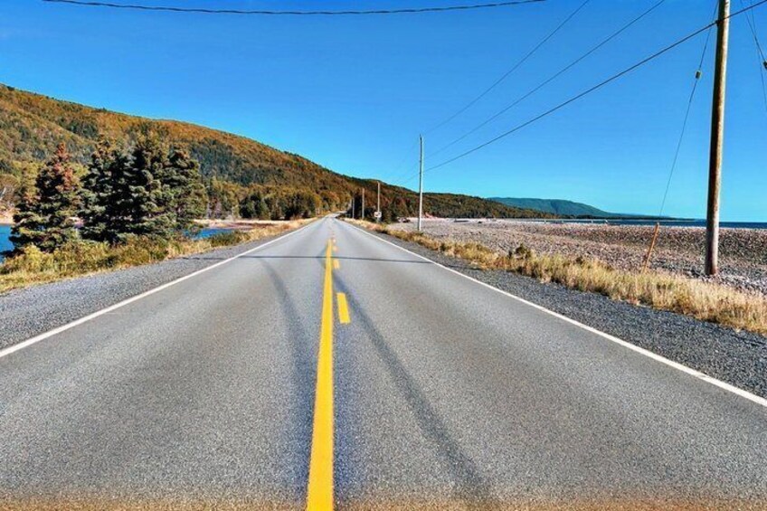 A two-lane road with yellow center lines, surrounded by hills and a clear sky. 3