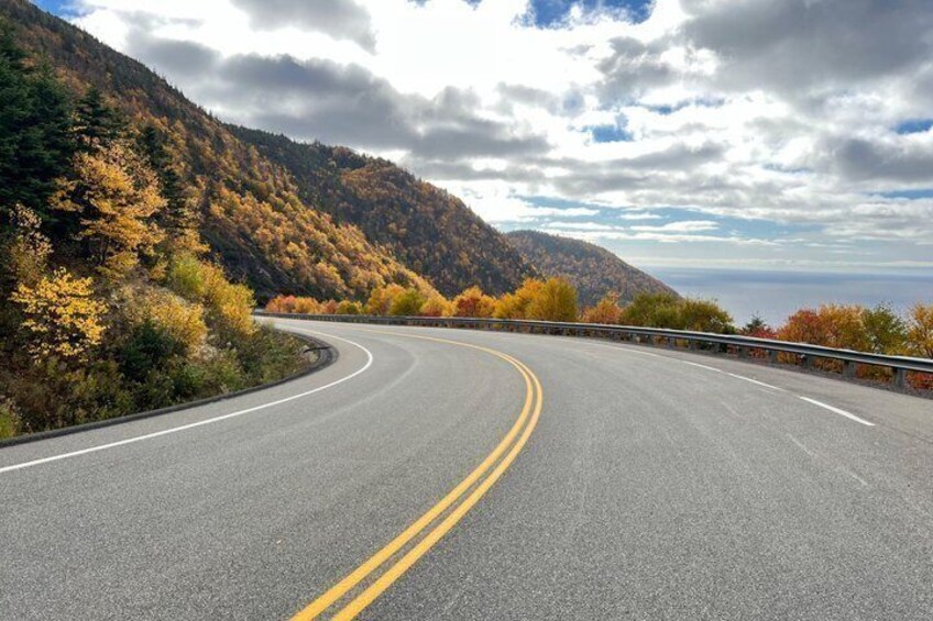 A winding road with a guardrail, surrounded by autumn-colored trees and hills. 5