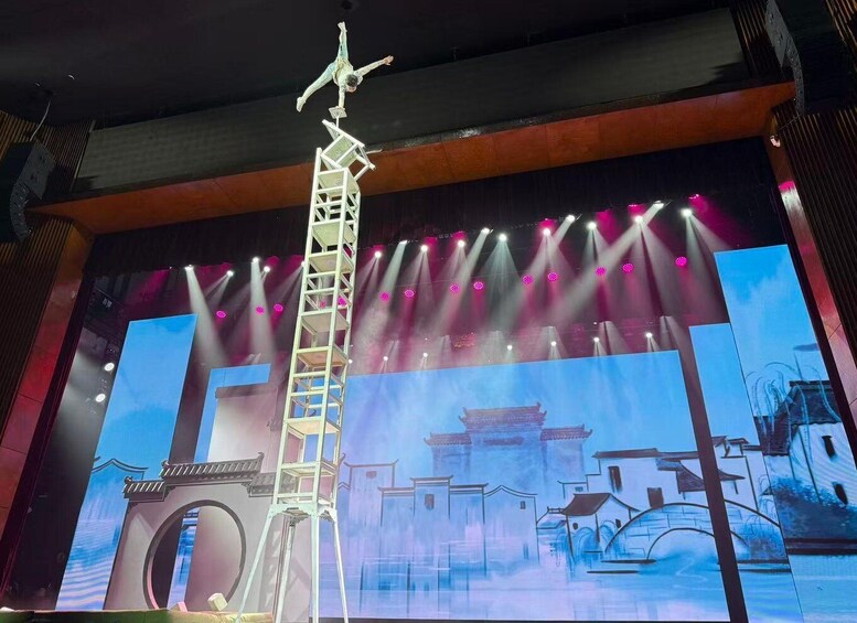 A stage with a performer on a ladder, a backdrop with traditional architecture, and stage lighting. 3