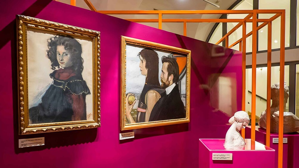 Two framed paintings on pink walls, with a sculpture on a pink pedestal. 2