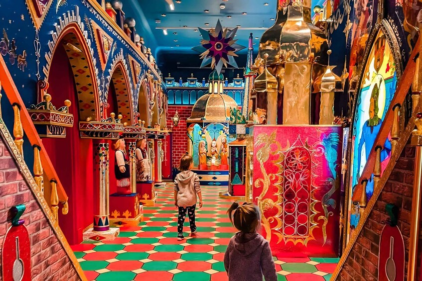 A colorful interior with a checkered floor, ornate decorations, and a child walking through. 1