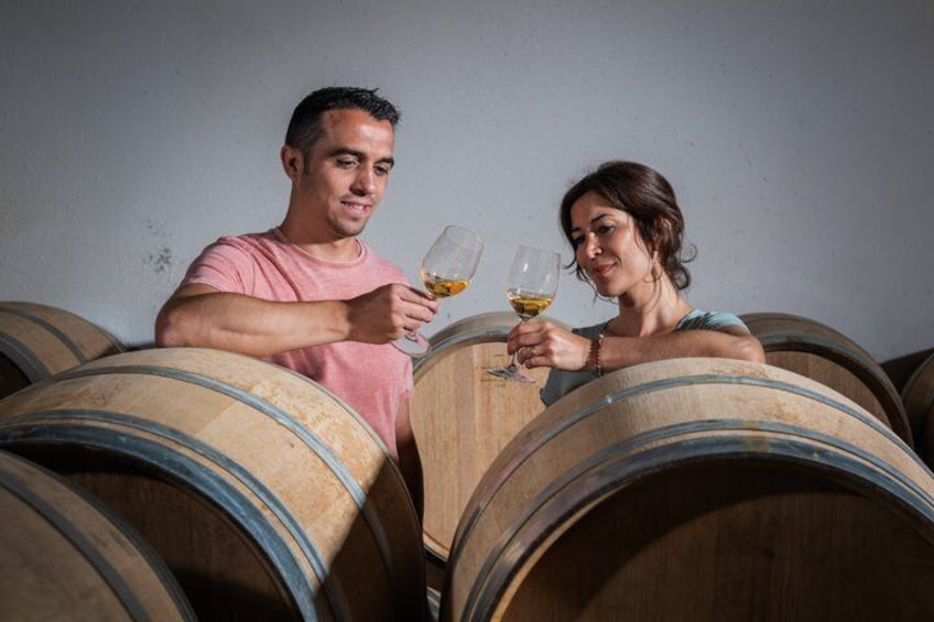 Deux personnes trinquent avec des verres de vin dans une cave où se trouvent des tonneaux en bois. 3