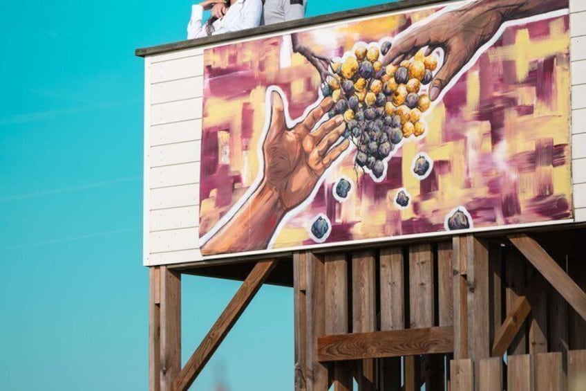 Une structure en bois ornée d’une fresque représentant des mains tenant des grappes de raisin. 4