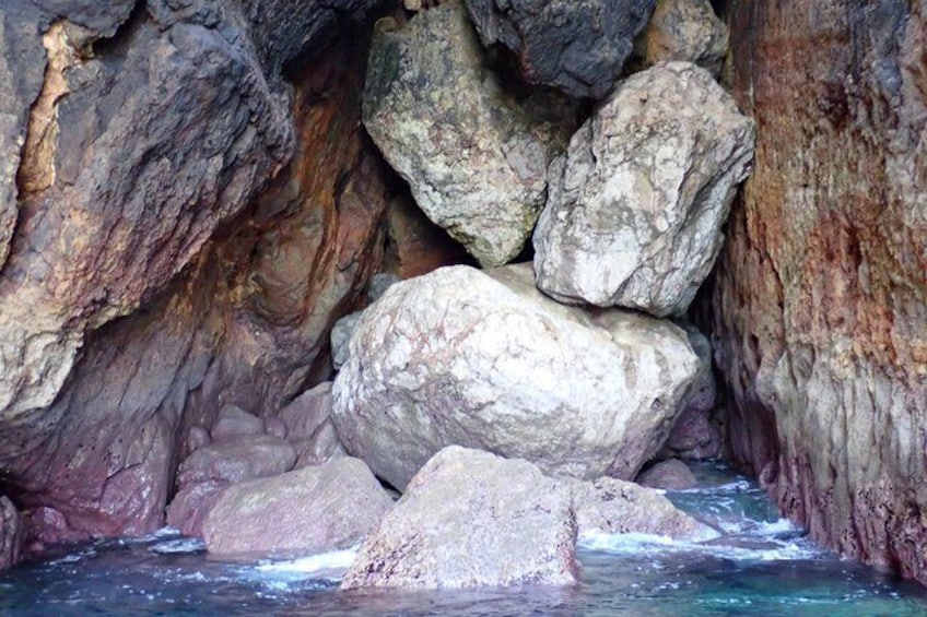 Eingang einer felsigen Höhle mit großen Felsbrocken und einem plätschernden Bach. 3