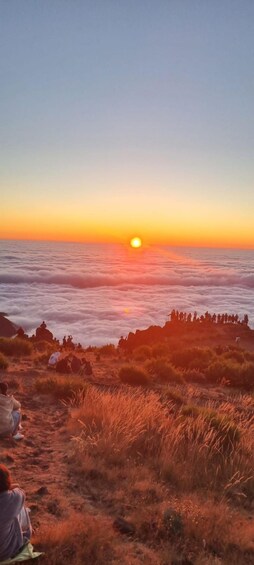 A sunset over a cloud-covered landscape with people observing the view. 1