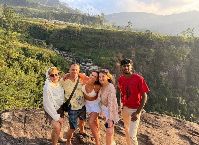 A group of people on a rocky outcrop overlooking a lush valley with a waterfall. 4