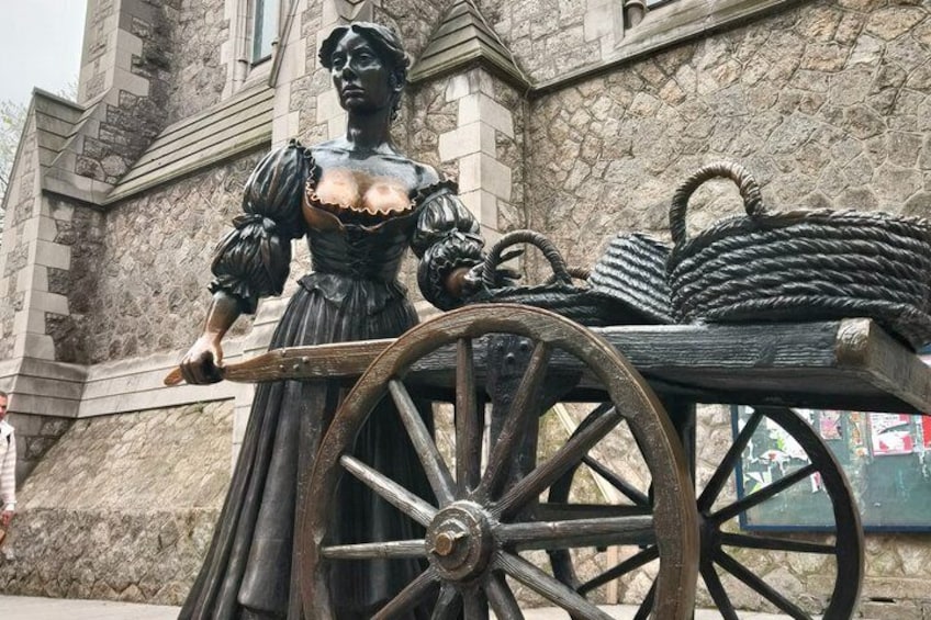 A statue of a woman in period attire next to a wooden cart with ropes. 3