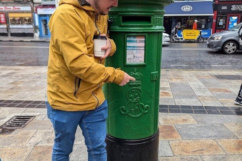 A person in a yellow jacket interacting with a green trash bin on a city sidewalk. 5