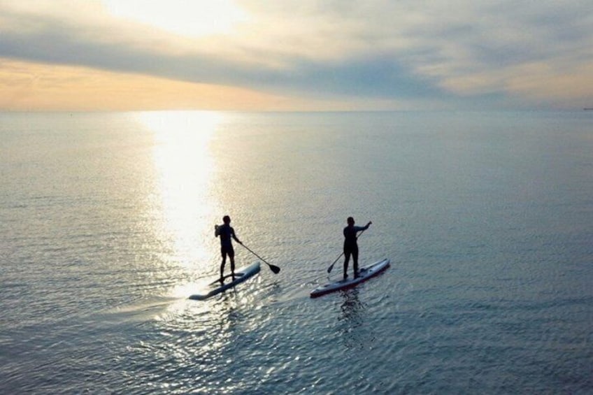 Two people paddleboarding on a calm sea during sunset. 2