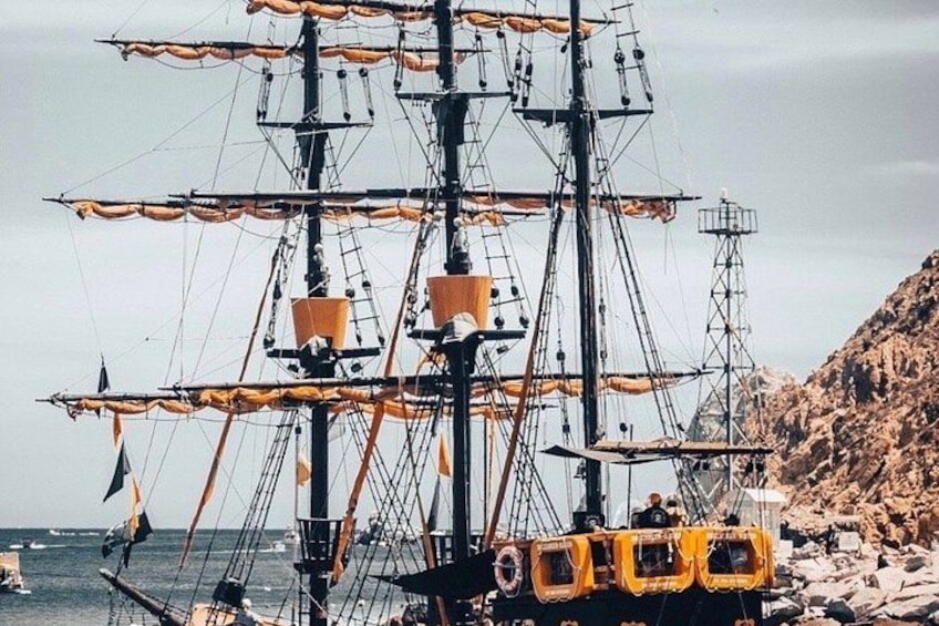 A large sailing ship with multiple masts and sails, anchored near rocky shores. 1