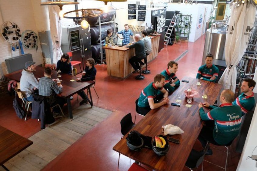 Un groupe de personnes se trouve dans un espace de restauration informel, avec une table en bois, des chaises et une cuisine en arrière-plan. 2